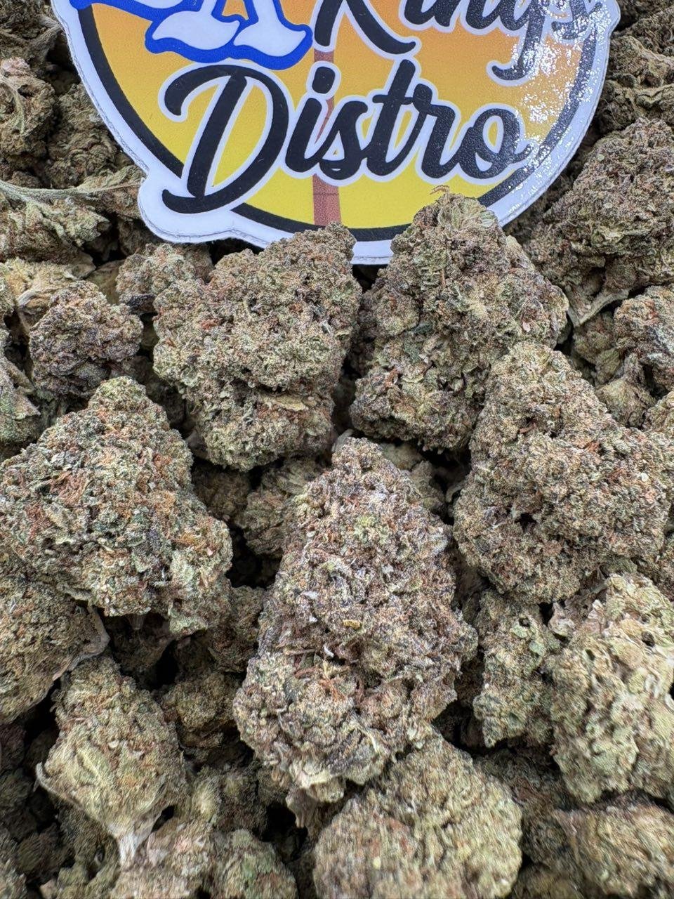 Frosty olive green and purple Gorilla Butter Lows cannabis buds beside the LA Kings Distro logo Frosty olive green and purple Gorilla Butter Lows cannabis buds beside the LA Kings Distro logo