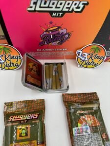 Open Sluggers Hit collectible tin showing five infused JUICED pre-rolls with Sluggers packaging in background